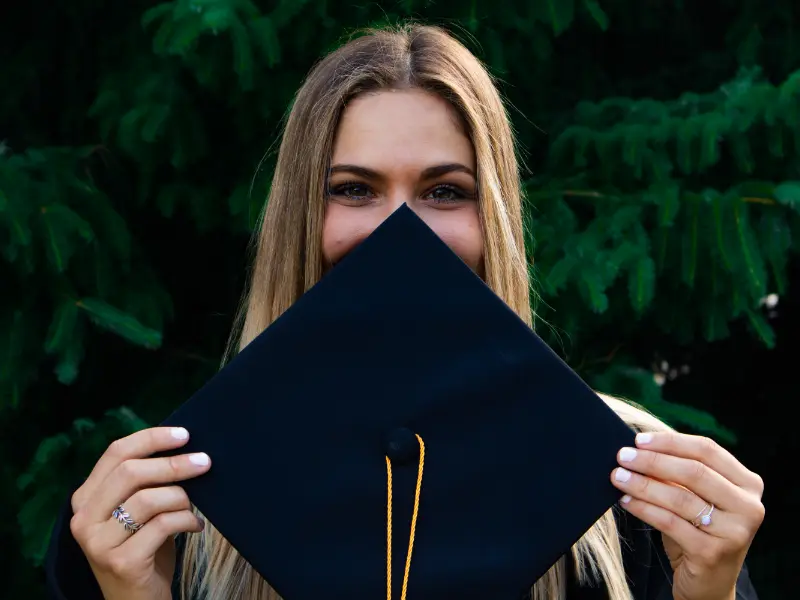 Studentin hält eine Abschlusskappe vor ihr Gesicht