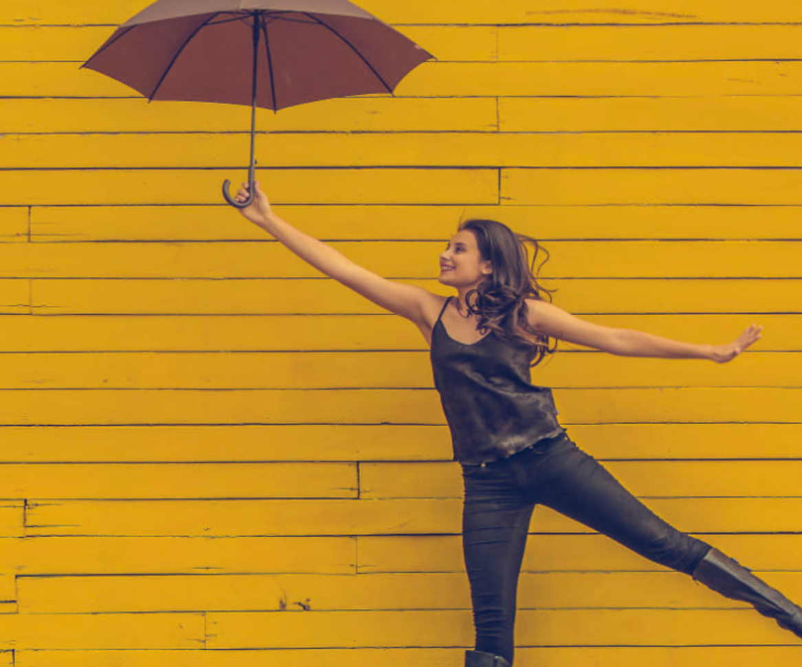 Frau hält Regenschirm von sich weg vor gelber Wand