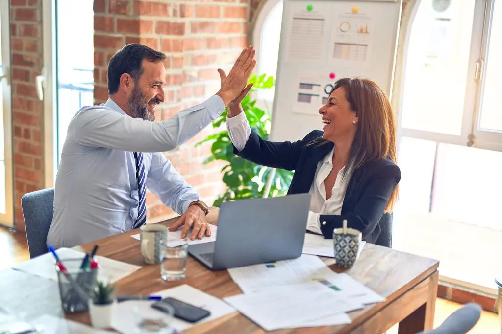 Zwei Geschäftsleute geben sich in einem Büro gegenseitig High Fives.