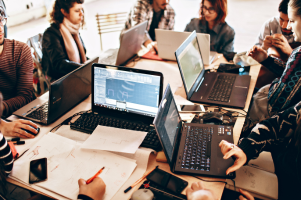 Eine Gruppe von Menschen sitzt mit Laptops an einem Tisch.