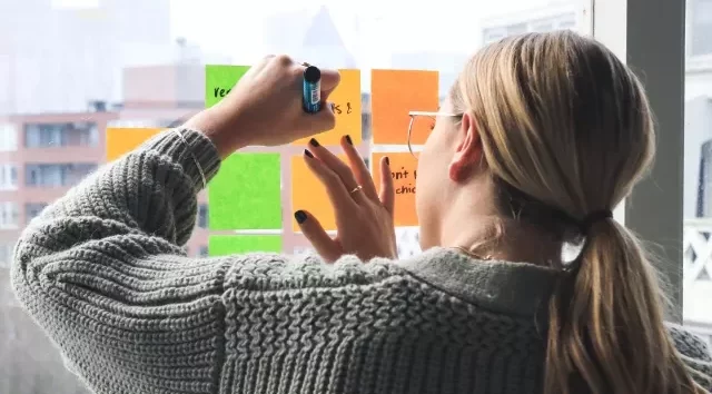 Studentin schreibt Post-its auf Glaswand