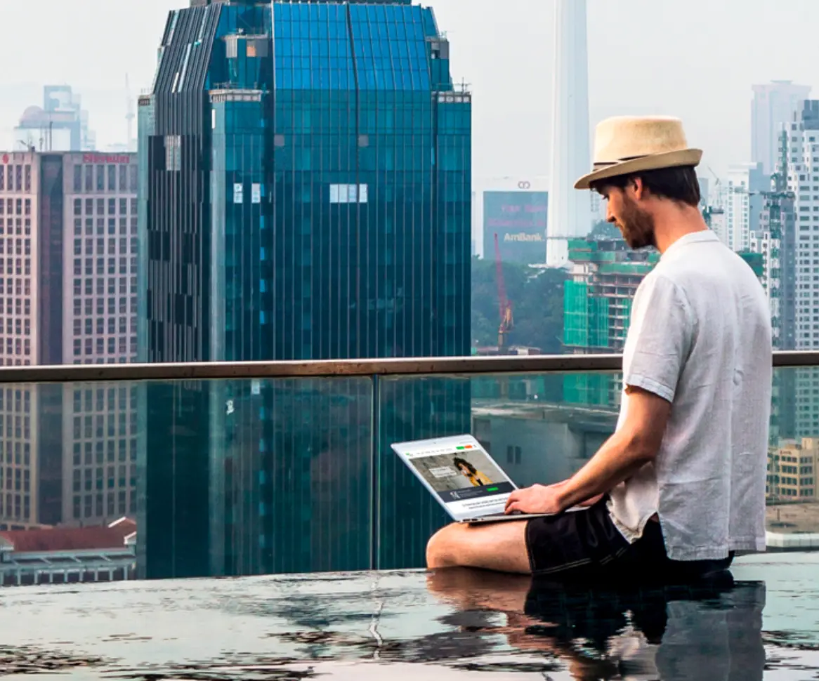 Student sitzt auf dem Rand eines Infinitypools am Laptop