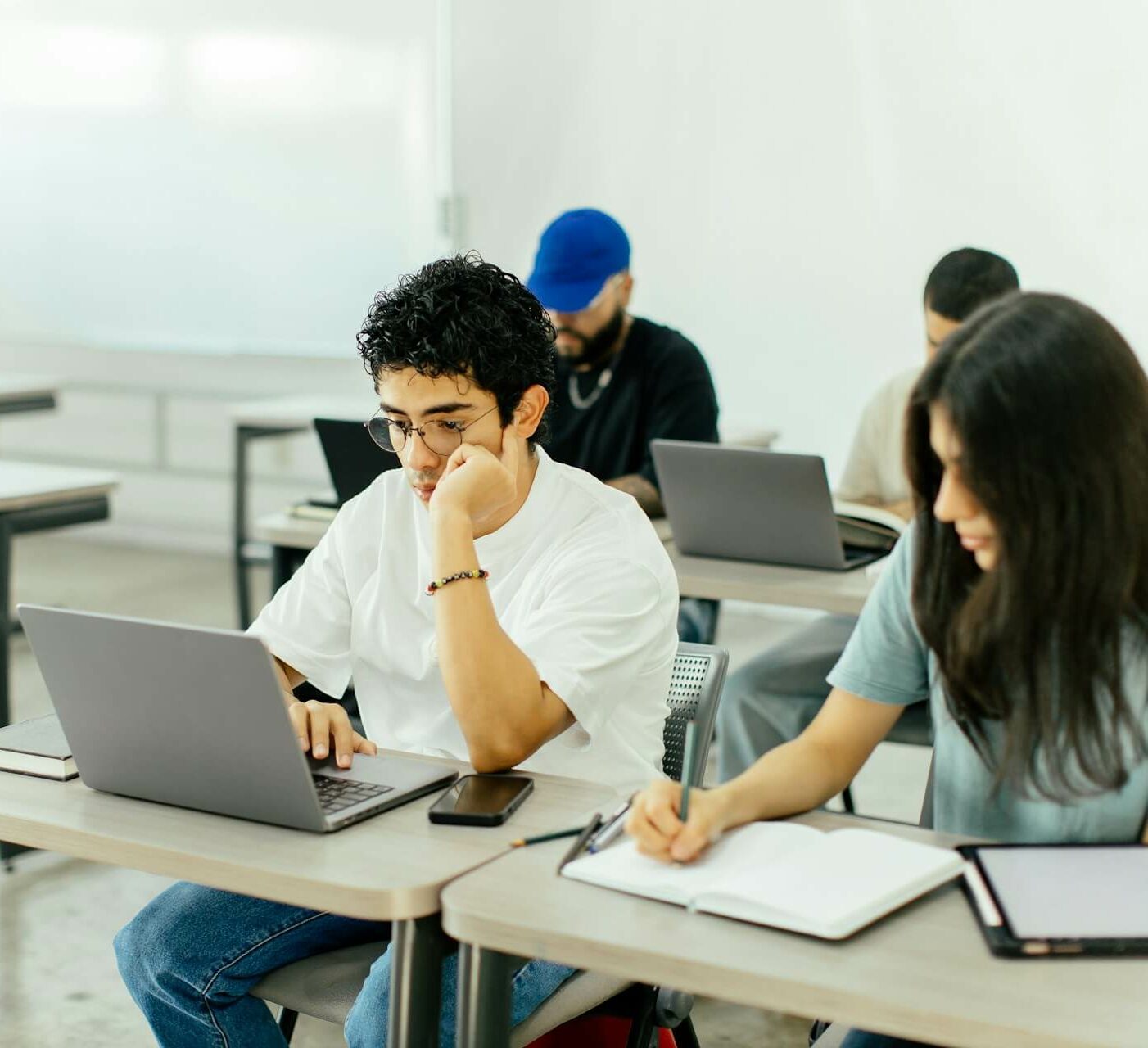 Das Bild zeigt eine Gruppe von Studenten, die in einem Klassenzimmer an ihren Laptops und Notizbüchern arbeiten.