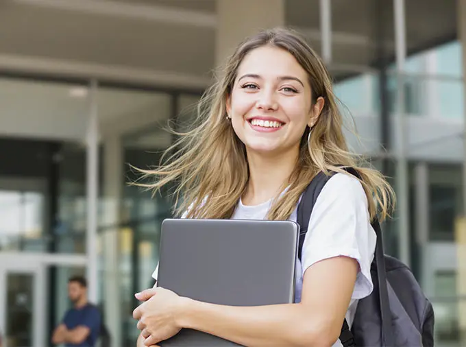 Studentin hat ihren Laptop in der Hand und steht vor einem Gebäude