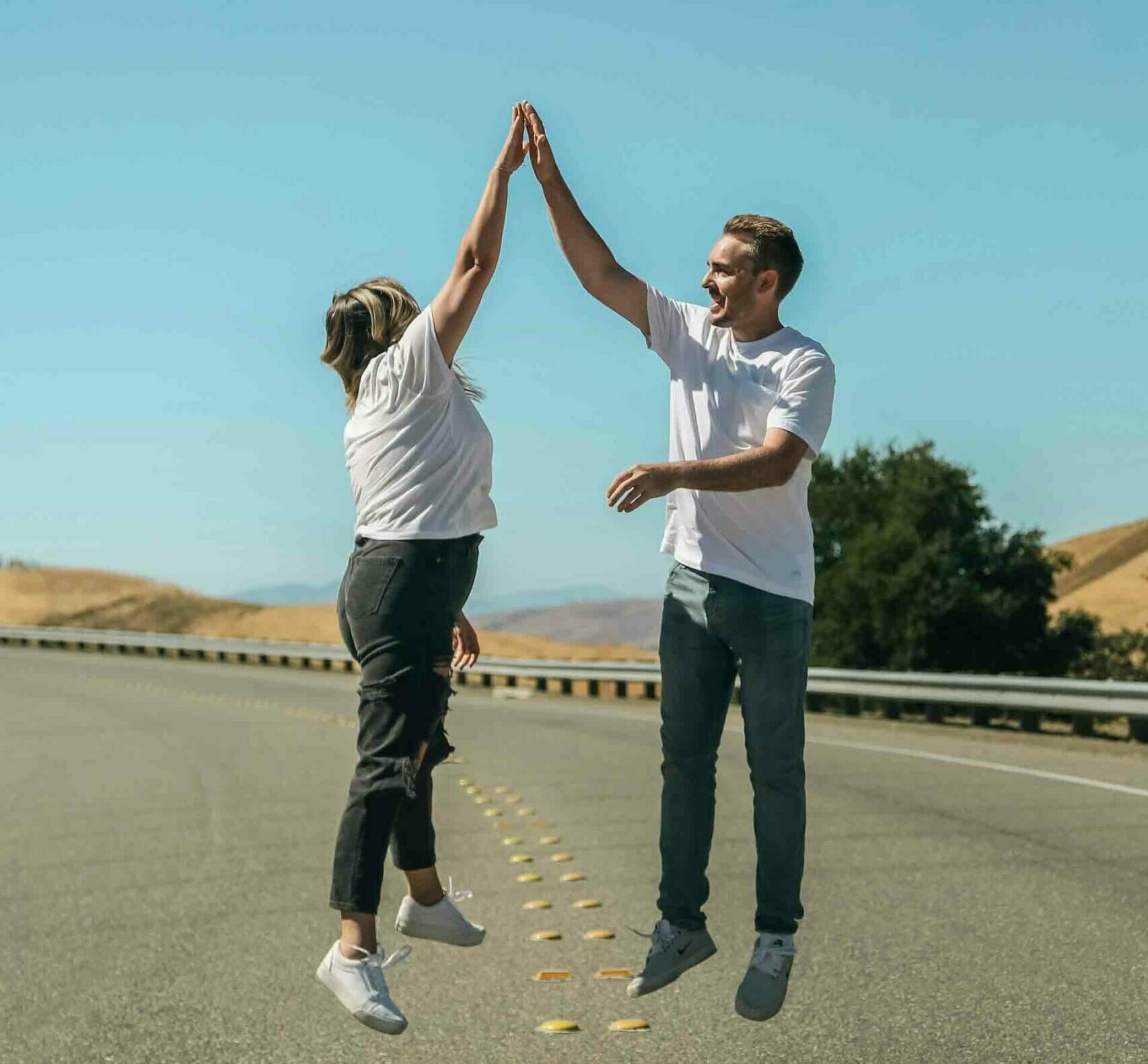Studierende geben sich ein High-Five auf einer Landstraße unter blauem Himmel