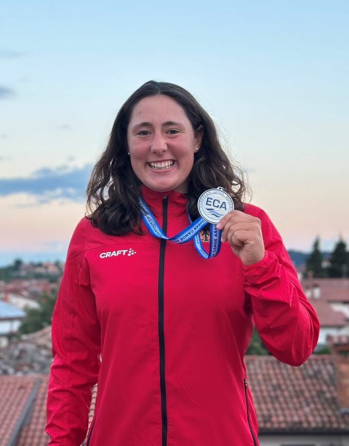 Paulina Pirro in rotem Craft-Trainingsanzug hält ECA-Medaille, im Hintergrund italienische Landschaft mit Dächern und Abendhimmel
